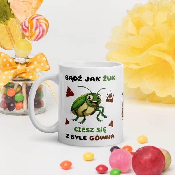 Śmieszny kubek z napisem Bądź jak Żuk ciesz się z byle gówna oraz grafiką zabawnego żuka Mega Prezencik
